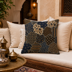 An intricate bohemian batik pattern throw pillow styled on a cream-colored sofa in a warm, textured Moroccan-style living room with antique brass tableware in the foreground.