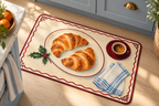 Christmas Croissant Breakfast Printed Floor Mat, lifestyle view 4: Close overhead-oblique view of one mat on a clean pale-wood floor near a cabinet, all four corners in frame, soft side light reveals short flannel nap.