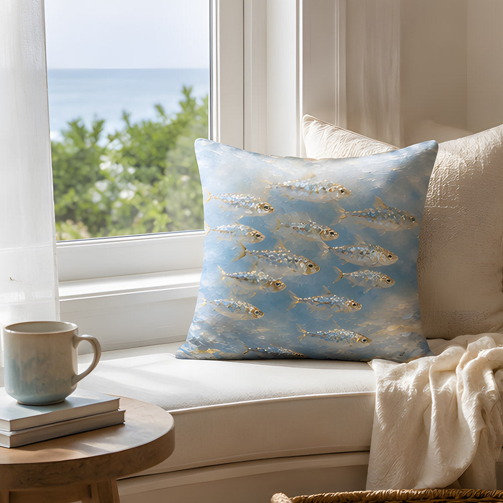 A coastal ocean-inspired throw pillow placed on a sunlit white window seat overlooking the blue sea, paired with a ceramic coffee mug, books, and a soft throw blanket.