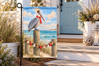 Coastal Pelican Christmas Printed Garden Flag, lifestyle view 1: One flag on a simple separate black L-shaped garden stake beside a front porch planter, all of the flag readable, late-afternoon natural light.