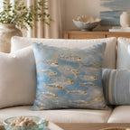 An artistic coastal style fish print throw pillow styled on a modern cream fabric sofa, surrounded by neutral linen cushions, with soft curtains and green branches in the background.