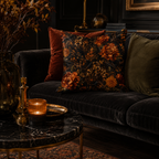 A luxurious dark baroque floral and cheetah print throw pillow styled on a vintage black velvet sofa, accompanied by amber glass candle holders, dark wood paneling, and warm candlelight.