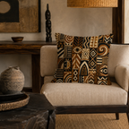 A detailed tribal totem patterned throw pillow placed on a neutral fabric accent chair with a dark wood frame, with a primitive African wooden statue on the console table behind.