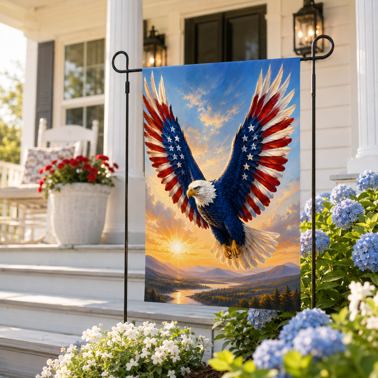 Soaring American eagle garden flag on a black stake positioned by white wooden porch steps and blooming blue hydrangea bushes.
