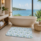 A tropical palm tree bath mat placed on a tiled floor next to a large freestanding bathtub in a luxury bathroom overlooking the ocean.