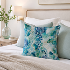 An elegant turquoise fluid art decorative pillow arranged on a luxury bed with premium cream-colored linens, accompanied by soft sage green pillows and a warm brass bedside lamp.