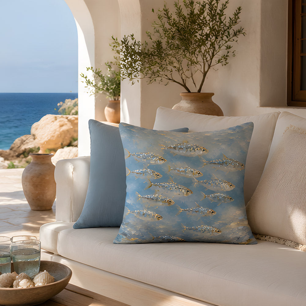 A Mediterranean style outdoor patio sofa overlooking the turquoise ocean, decorated with a blue marine fish printed pillow and a solid blue cushion, under a beautiful arched white wall.