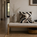 A minimalist fluid abstract patterned pillow resting on a sleek upholstered bench in an elegant entryway, accompanied by a ceramic vase with dried stems and a woven basket.