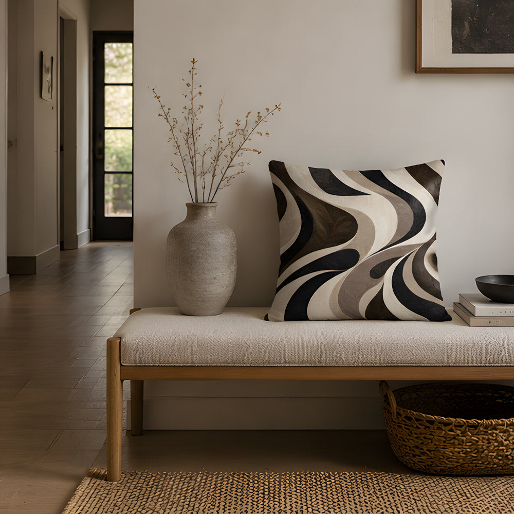A minimalist fluid abstract patterned pillow resting on a sleek upholstered bench in an elegant entryway, accompanied by a ceramic vase with dried stems and a woven basket.