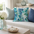 A luxury abstract agate fluid art throw pillow in vibrant turquoise and emerald green styled on a plush cream sofa, between soft blue and navy accent cushions, with a wooden coffee table in the foreground.
