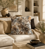 A modern abstract leopard and floral print decorative throw pillow styled on a plush cream-colored fabric sofa, surrounded by earthy ceramic vases, a rustic travertine coffee table, and warm sunlight.