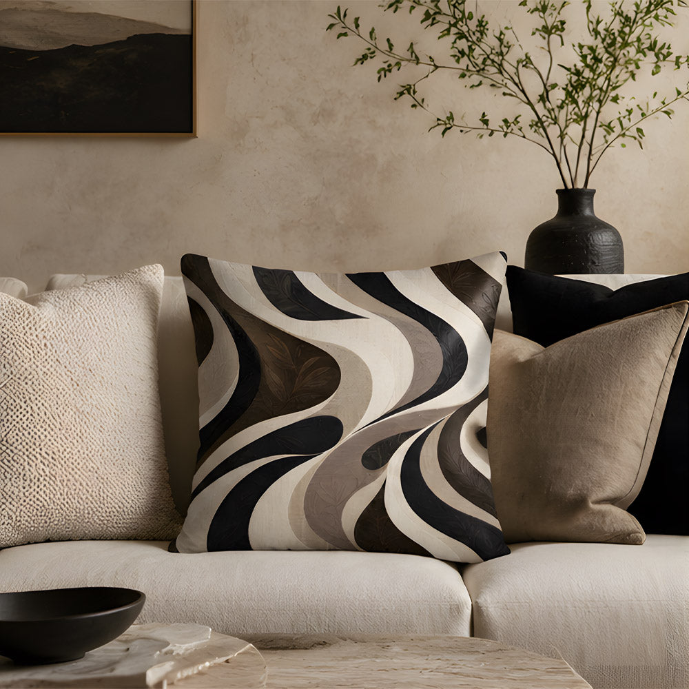 An artistic abstract wavy stripe throw pillow placed on a modern cream-colored fabric sofa, styled with textured cushions, a black ceramic vase with green branches, and a rustic stone coffee table.