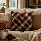A modern farmhouse style plaid throw pillow arranged on a plush cream-colored sofa, accessorized with neutral tone cushions, a glowing candle tray, and soft autumn floral decor.