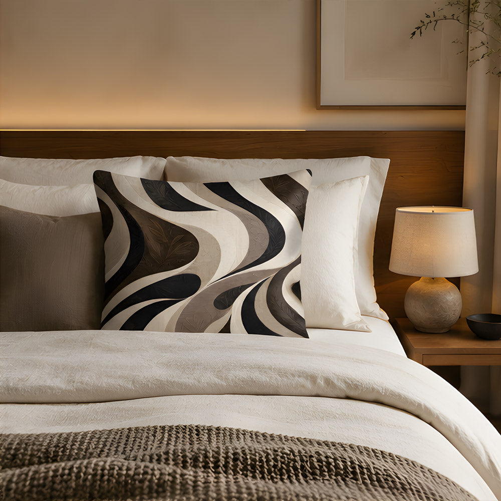 A modern fluid abstract wavy print throw pillow arranged on a luxury bed, featuring a rich wooden headboard, soft neutral linens, and a glowing bedside lamp.
