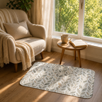 A soft botanical accent mat placed on a hardwood floor next to a cozy beige armchair and a wooden side table with a steaming coffee cup by a sunny window.