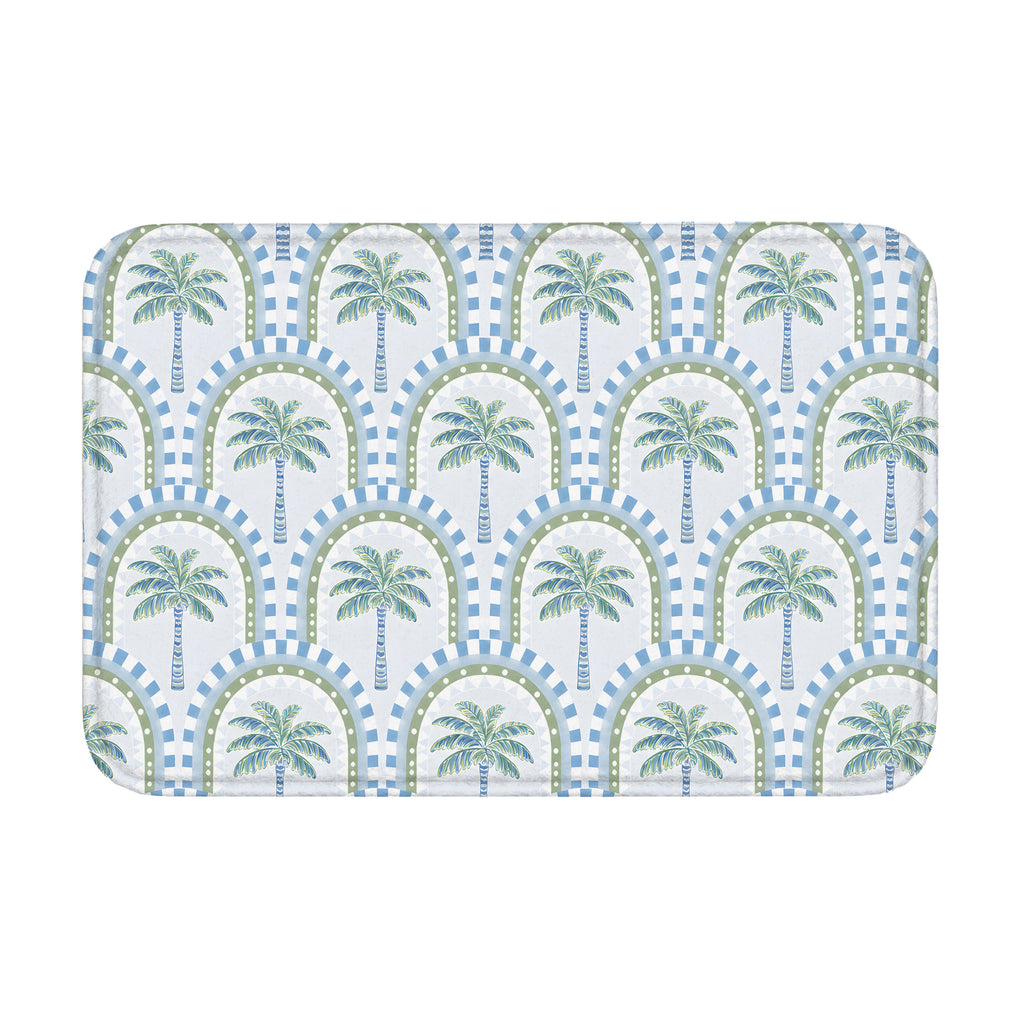 A rectangular bathroom mat featuring a repeating tropical palm tree and geometric arch pattern in soft blue and sage green colors on a white background.