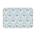 A rectangular bathroom mat featuring a repeating tropical palm tree and geometric arch pattern in soft blue and sage green colors on a white background.