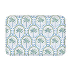 A rectangular bathroom mat featuring a repeating tropical palm tree and geometric arch pattern in soft blue and sage green colors on a white background.
