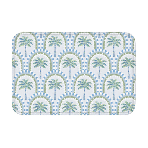 A rectangular bathroom mat featuring a repeating tropical palm tree and geometric arch pattern in soft blue and sage green colors on a white background.