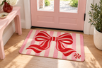 Peppermint Bow Christmas Printed Floor Mat, lifestyle view 1: One mat laid flat INSIDE the front door, full landscape mat and all four rounded corners visible at small accent-mat scale, angled downward photography.