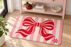 Peppermint Bow Christmas Printed Floor Mat, lifestyle view 4: Close overhead-oblique view of one mat on a clean pale-wood floor near a cabinet, all four corners in frame, soft side light reveals short flannel nap.