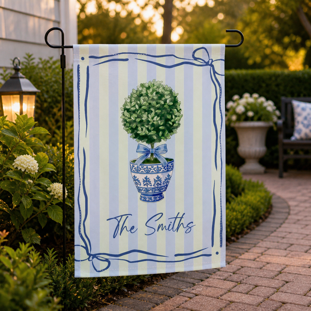 Personalized topiary garden flag displayed along a warm garden walkway