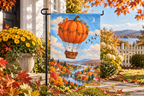 Pumpkin Hot Air Balloon Printed Garden Flag, lifestyle view 1: One flag on a simple separate black L-shaped garden stake beside a front porch planter, all of the flag readable, late-afternoon natural light.