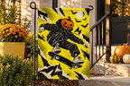 Pumpkin Skateboard Printed Garden Flag, lifestyle view 1: One flag on a simple separate black L-shaped garden stake beside a front porch planter, all of the flag readable, late-afternoon natural light.