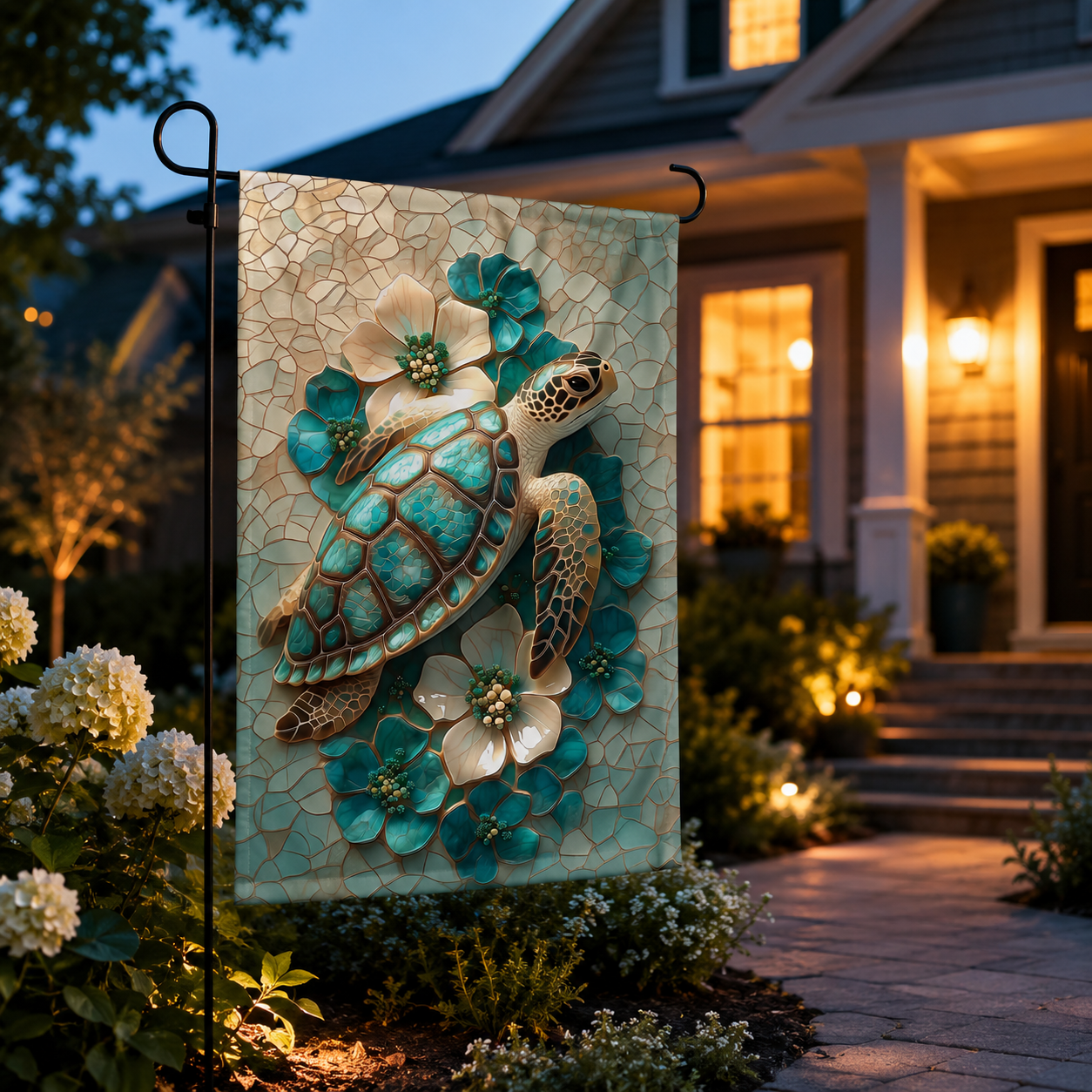 Sea turtle floral garden flag displayed at dusk near a warmly lit front porch, with white hydrangeas and pathway lights.