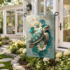 Sea turtle floral garden flag displayed outside a white cottage, with turquoise flowers, white blooms, and soft garden light.
