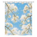 Front view of a white fabric shower curtain with a vibrant print of white tree blossoms against a bright blue sky with fluffy clouds.