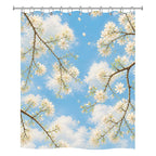 Front view of a white fabric shower curtain with a vibrant print of white tree blossoms against a bright blue sky with fluffy clouds.