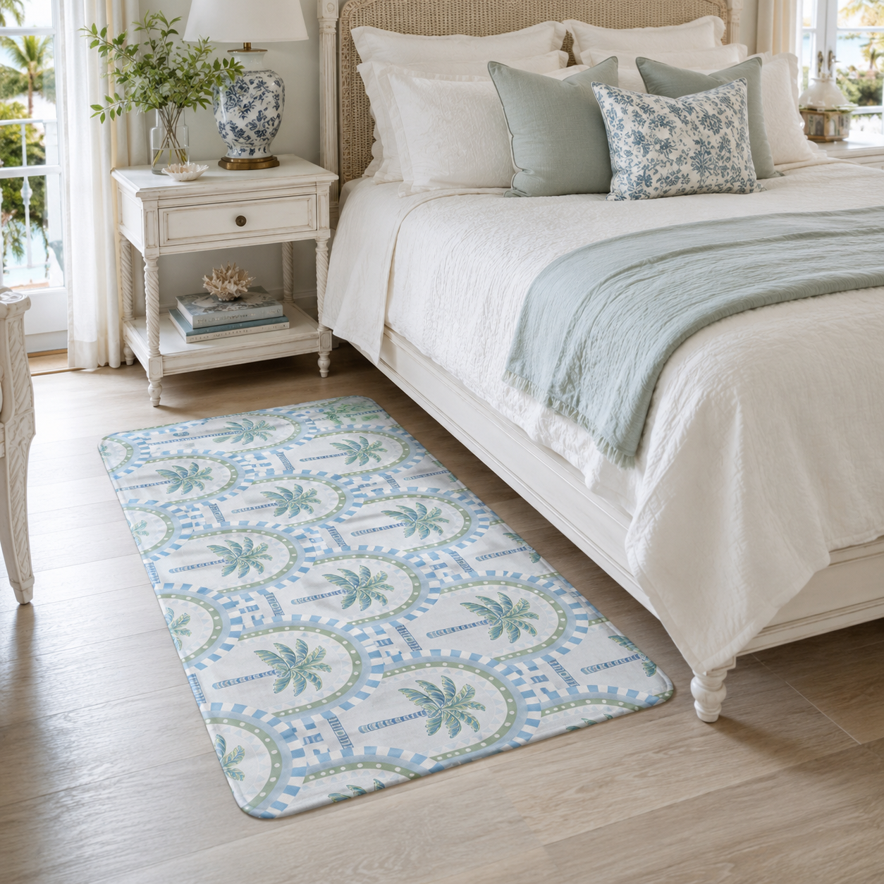 A large palm tree and arch patterned accent rug placed on a light wooden floor next to a cozy white and sage green themed bed.