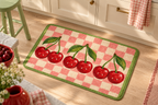 Vampire Cherry Check Printed Floor Mat, lifestyle view 4: Close overhead-oblique view of one mat on a clean pale-wood floor near a cabinet, all four corners in frame, soft side light reveals short flannel nap.